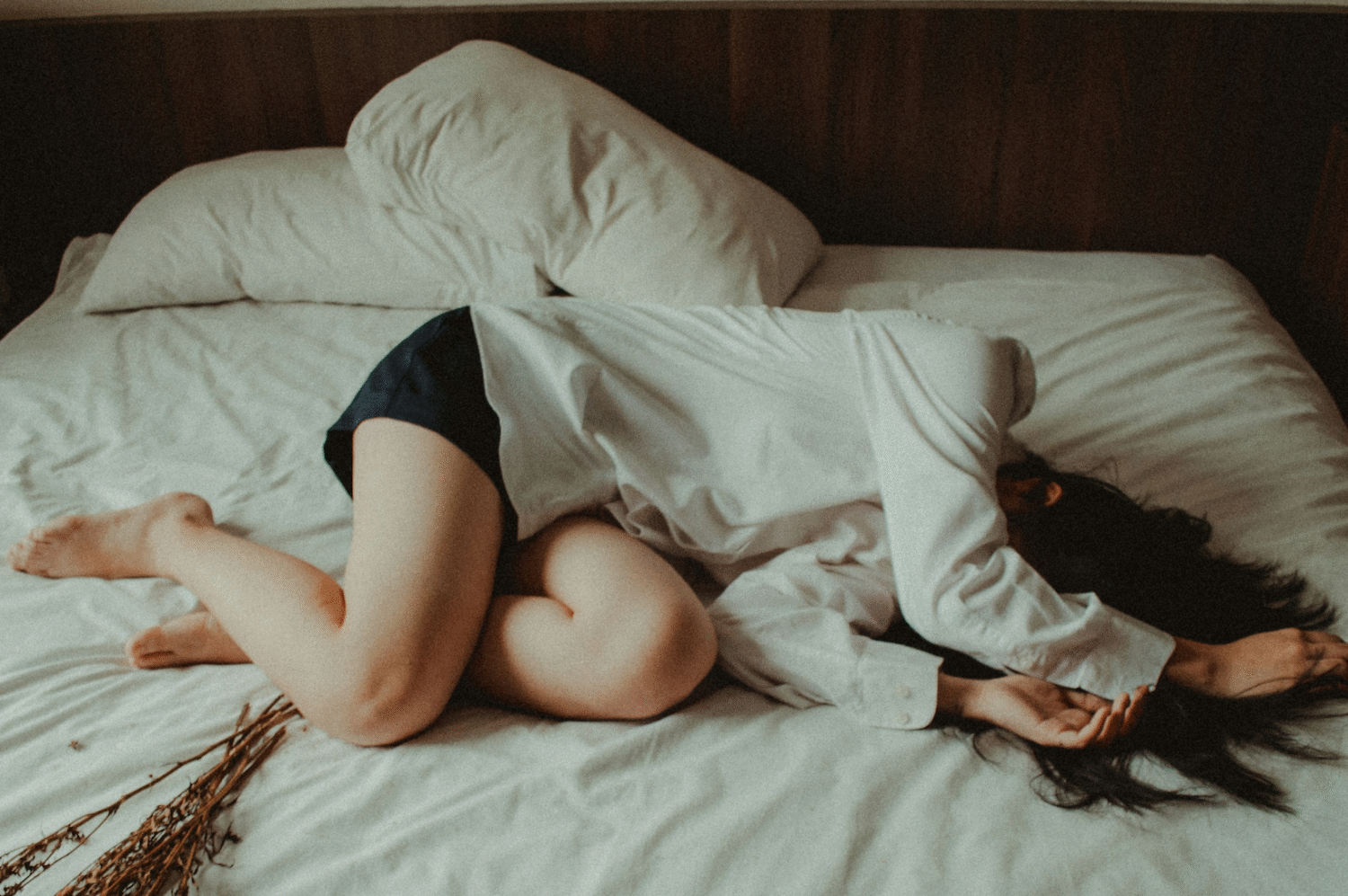 Women lying on bed white sheets in fetal position hands covering face