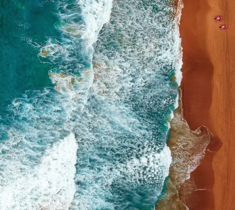 An aerial view of turquoise ocean waves crashing onto a warm sandy beach