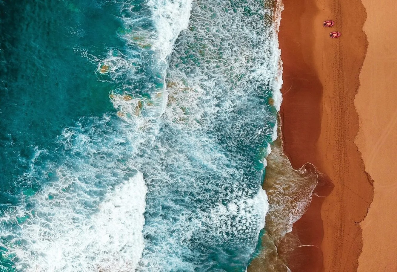 An aerial view of turquoise ocean waves crashing onto a warm sandy beach