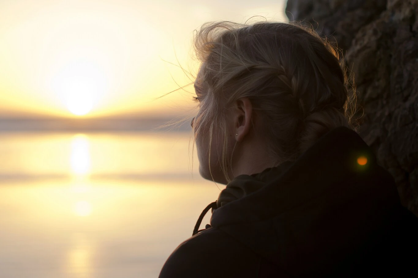 A woman looking toward the ocean at sunset.