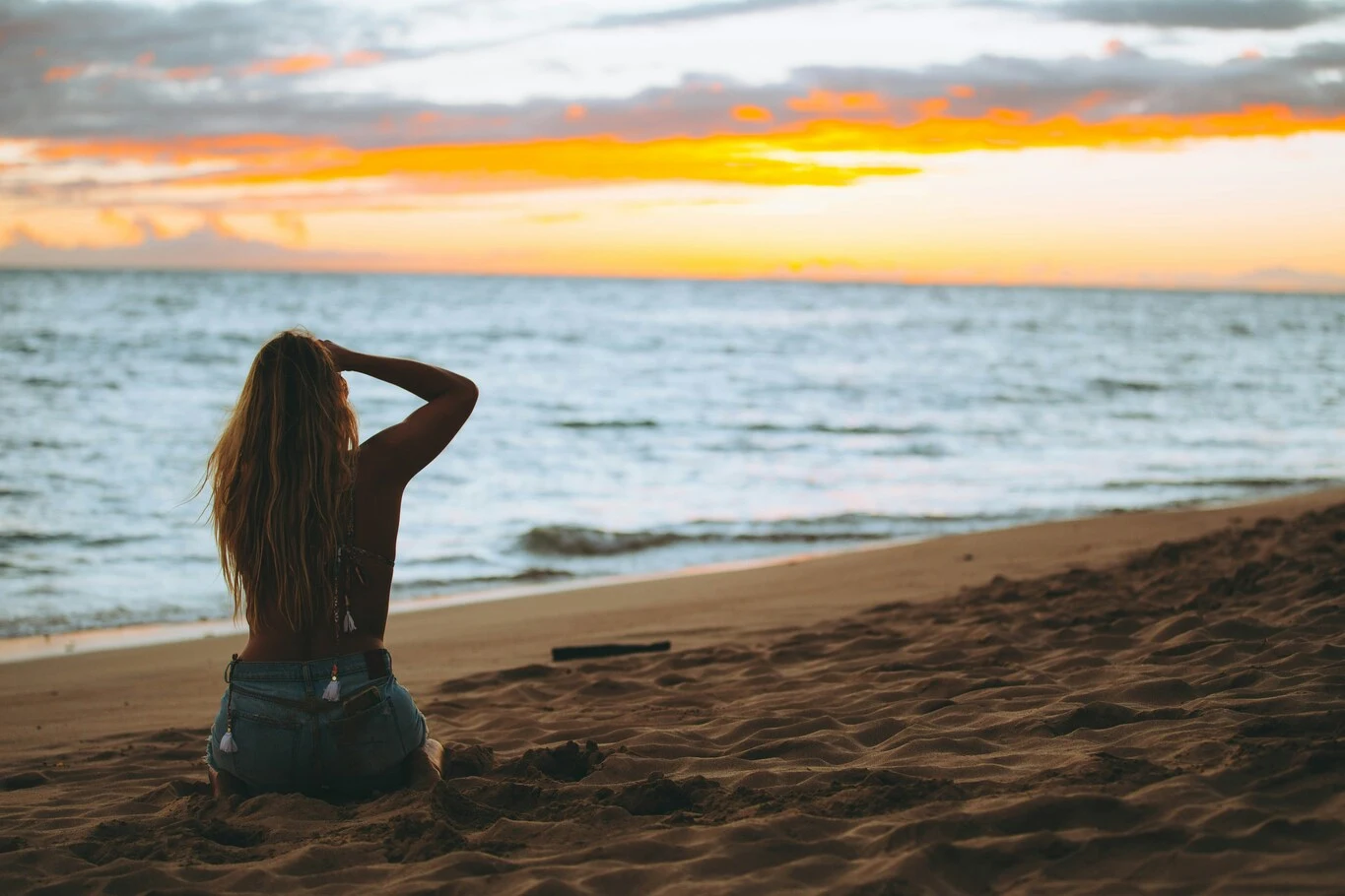 Woman sitting on a beach looking at the ocean during sunset