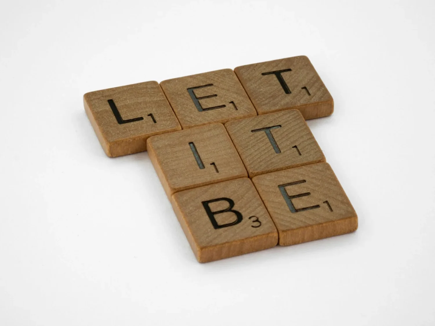 Wooden letter tiles spelling "LET IT BE" on a white surface.