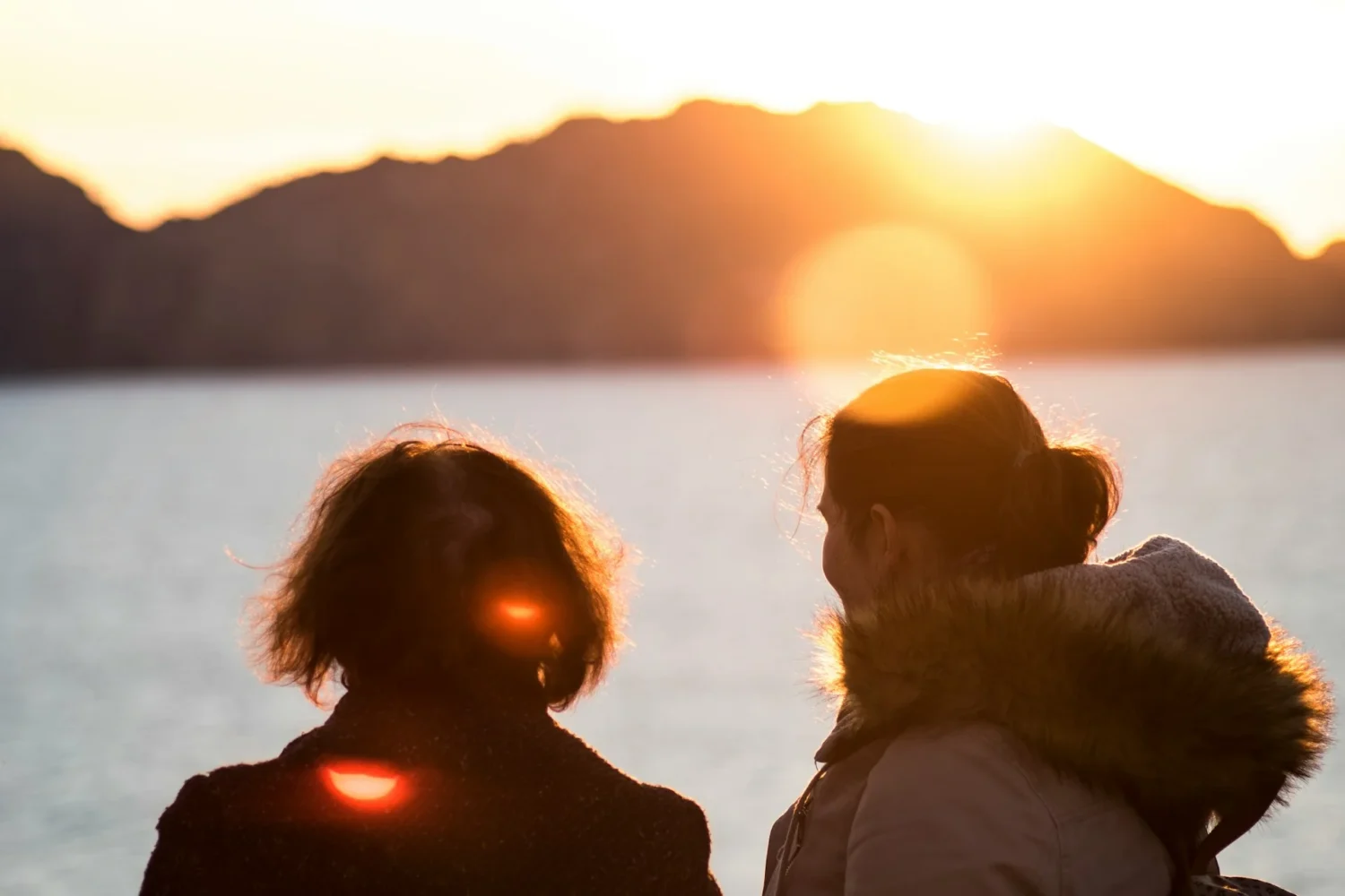Two people facing into the sunset overlooking the water
