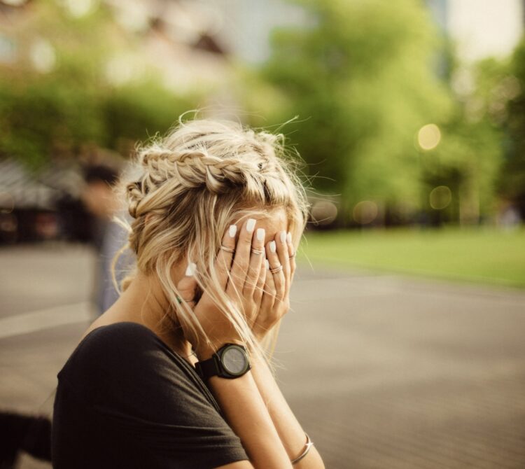 A woman sitting in a park with her hands over her face in relation to depression after breakup