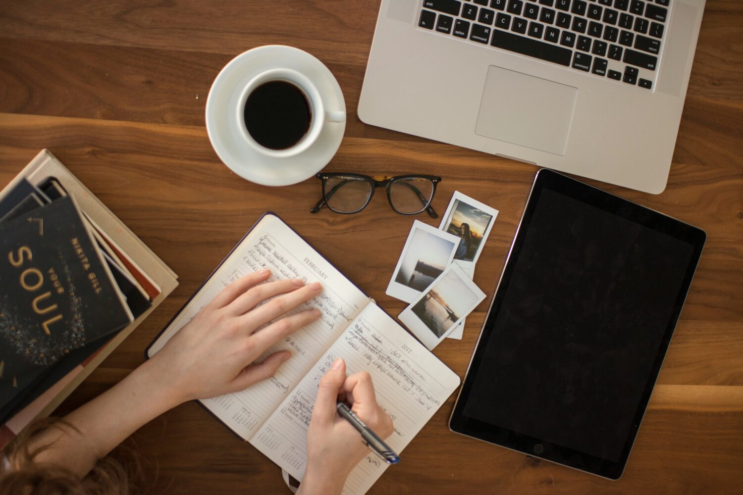 Work desk with laptop, cup of coffee, glasses, photos and hands writing in a diary/planner