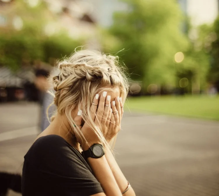 A woman sitting in a park with her hands over her face