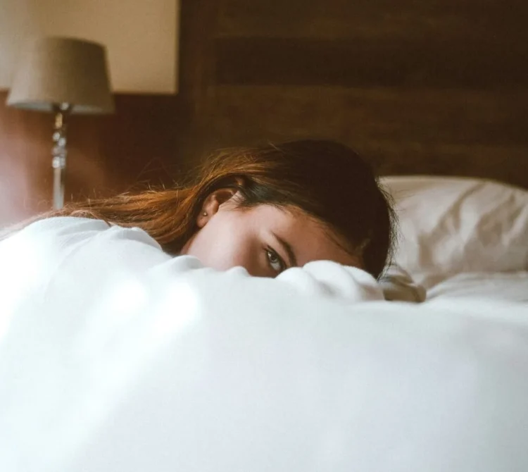 Woman leaning on bed with part of her face covered