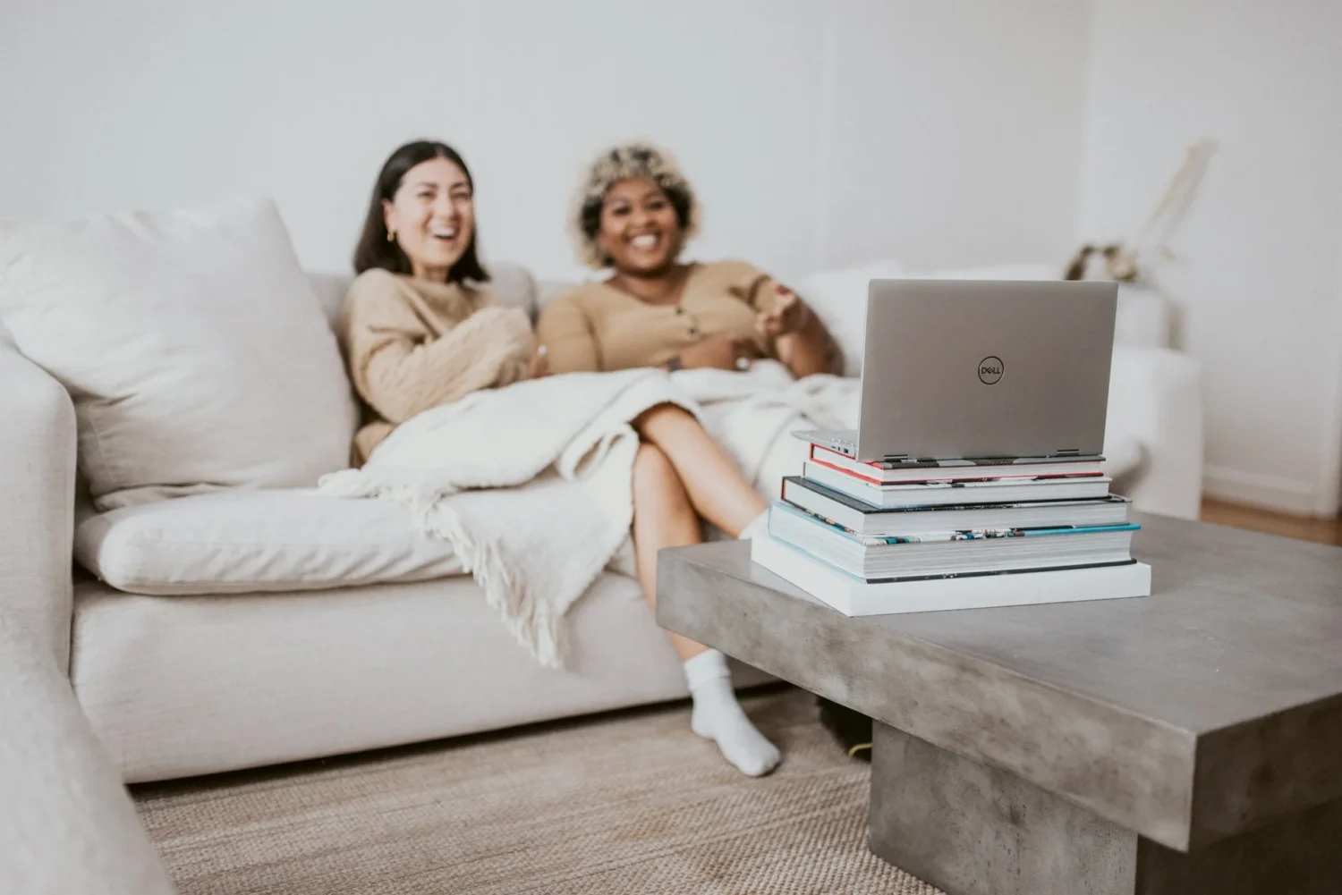 Two women sitting on a couch smiling and looking at a laptop