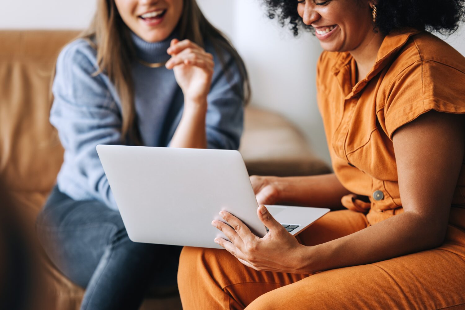 two women sitting on a couch looking at a computer smiling