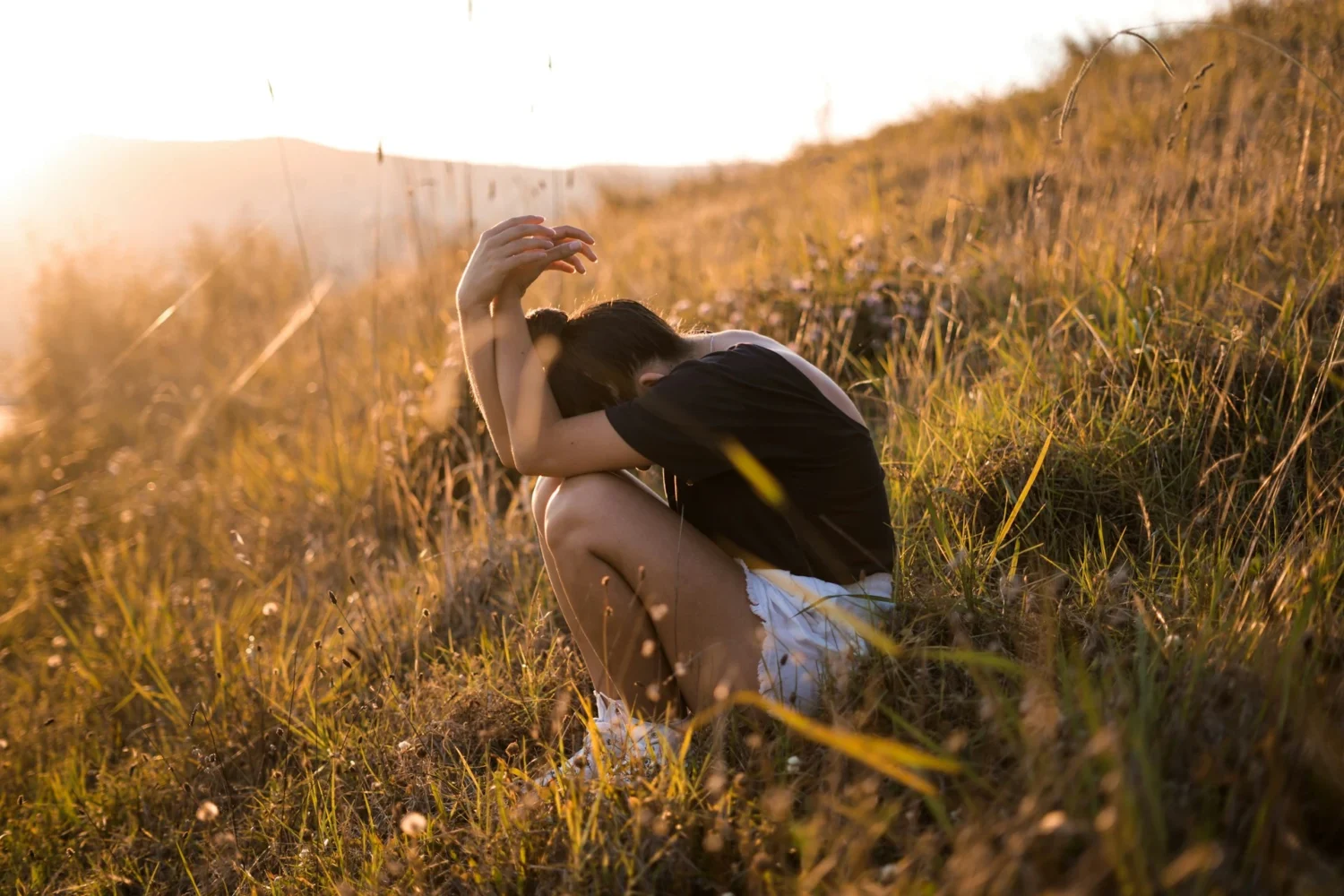 A woman sitting on the ground in a paddock with her hands over her head