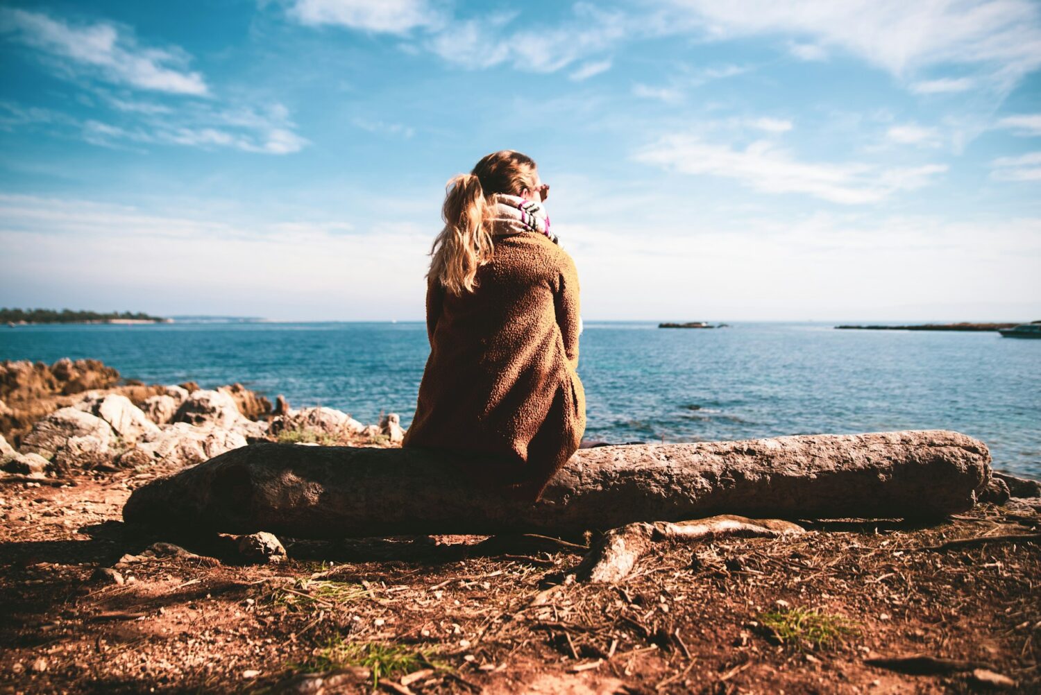A woman sitting on a log overlooking the ocean