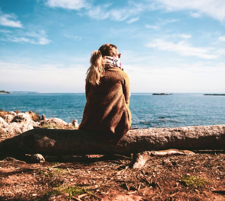 A woman sitting on a log overlooking the ocean