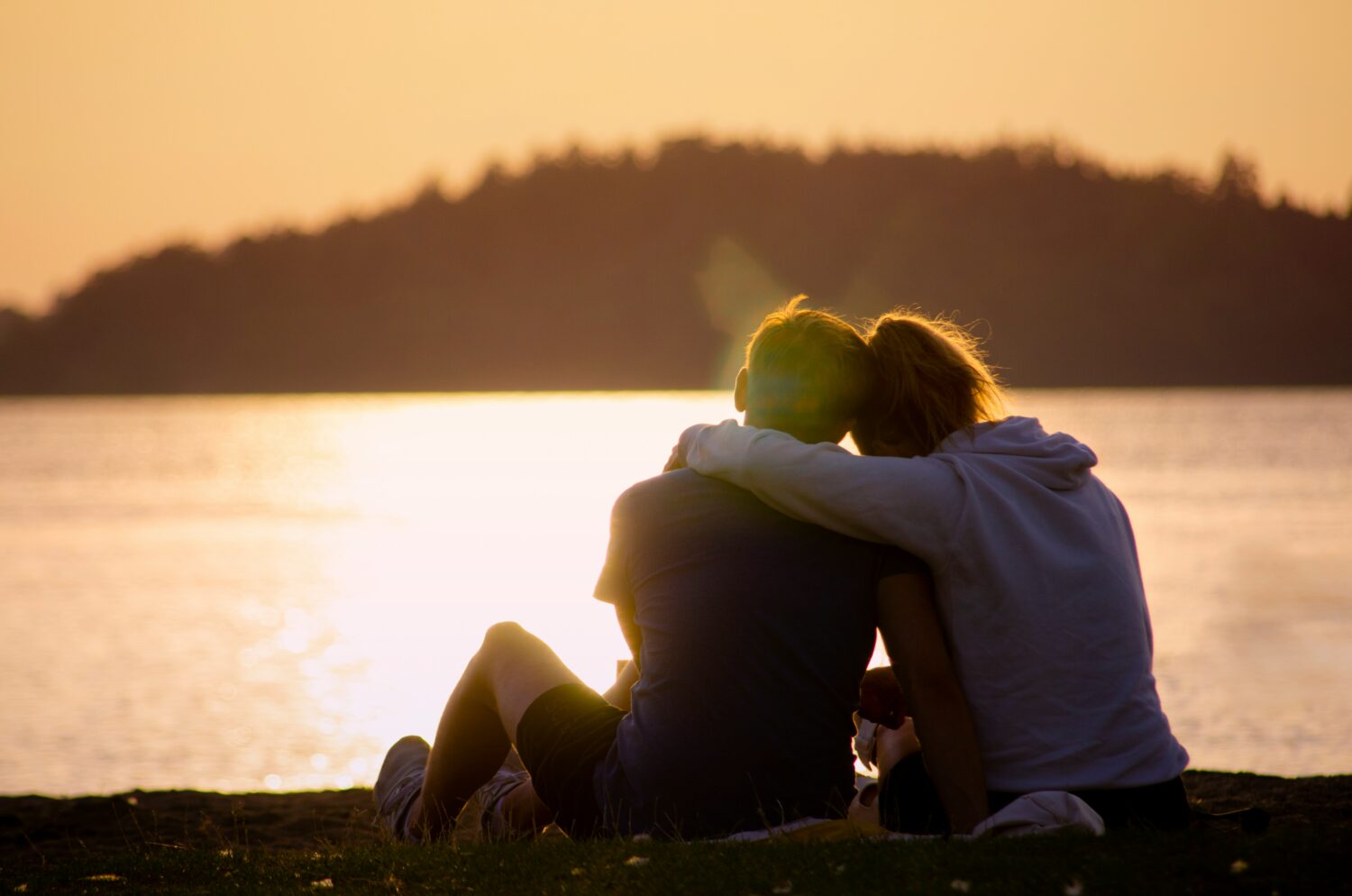 Two people sitting by lake durning sunset with arms wrapped around one another