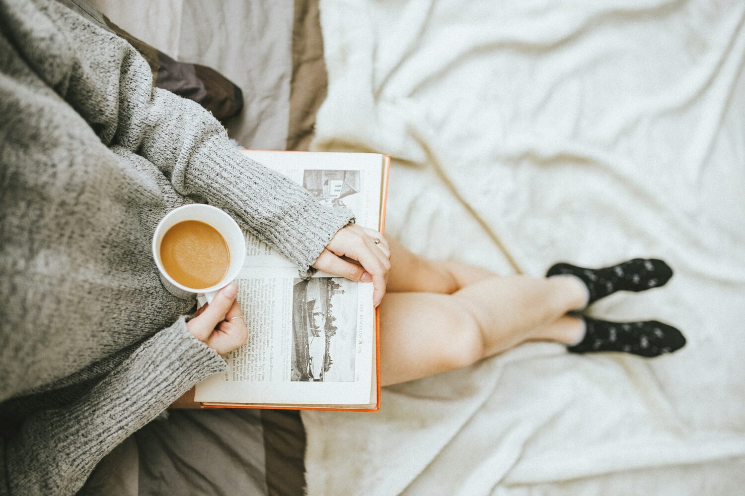A person sitting reading a book with a cup of coffee