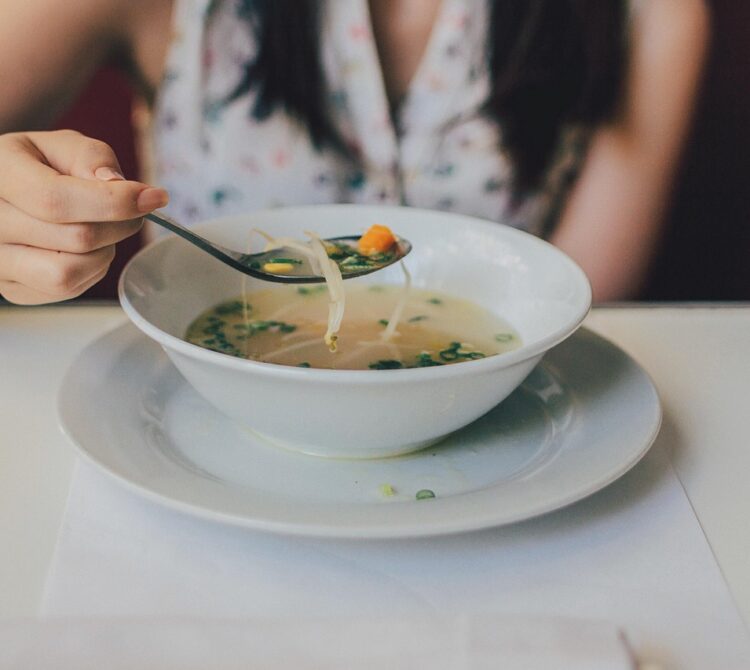 A person eating a bowl of chicken noodle soup