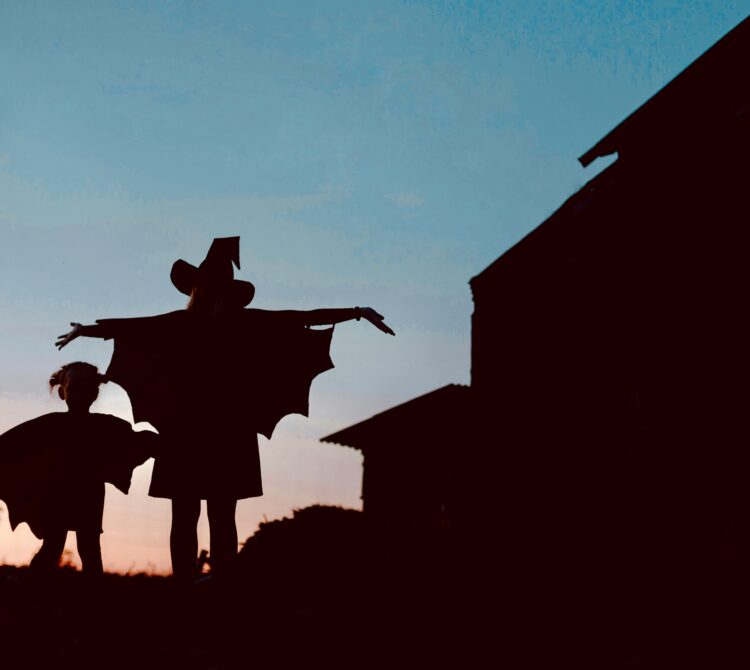 A silhouette of a child and teenager wearing Halloween costumes against a sunset