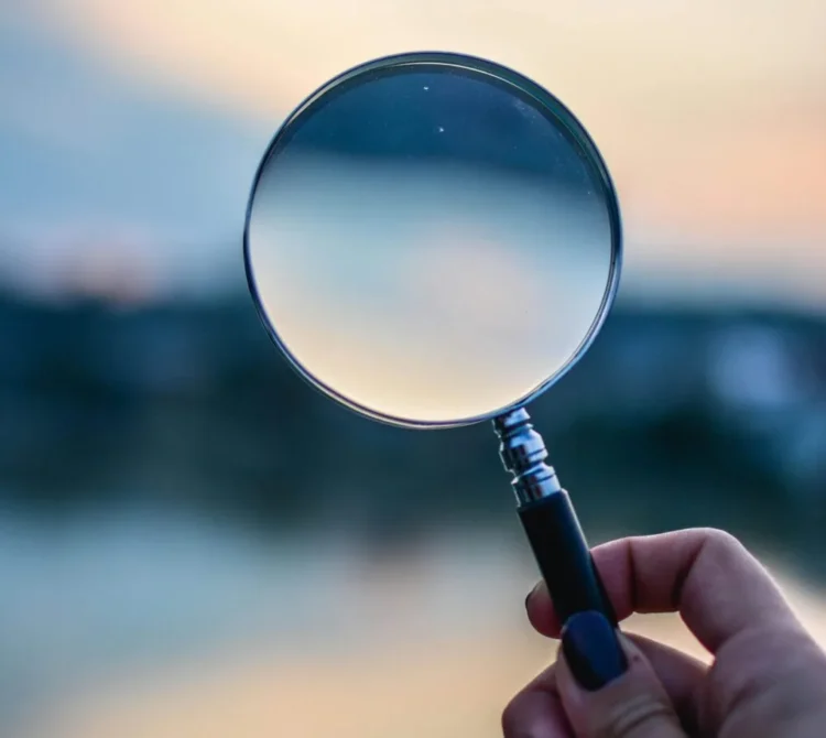 A person holding a magnifying glass outdoors against a soft, golden-hour background,,