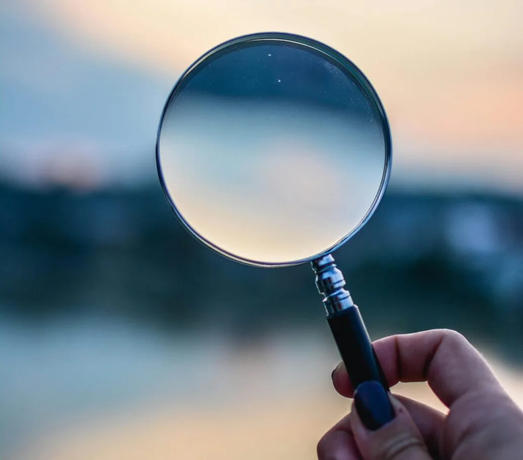 A person holding a magnifying glass outdoors against a soft, golden-hour background,,