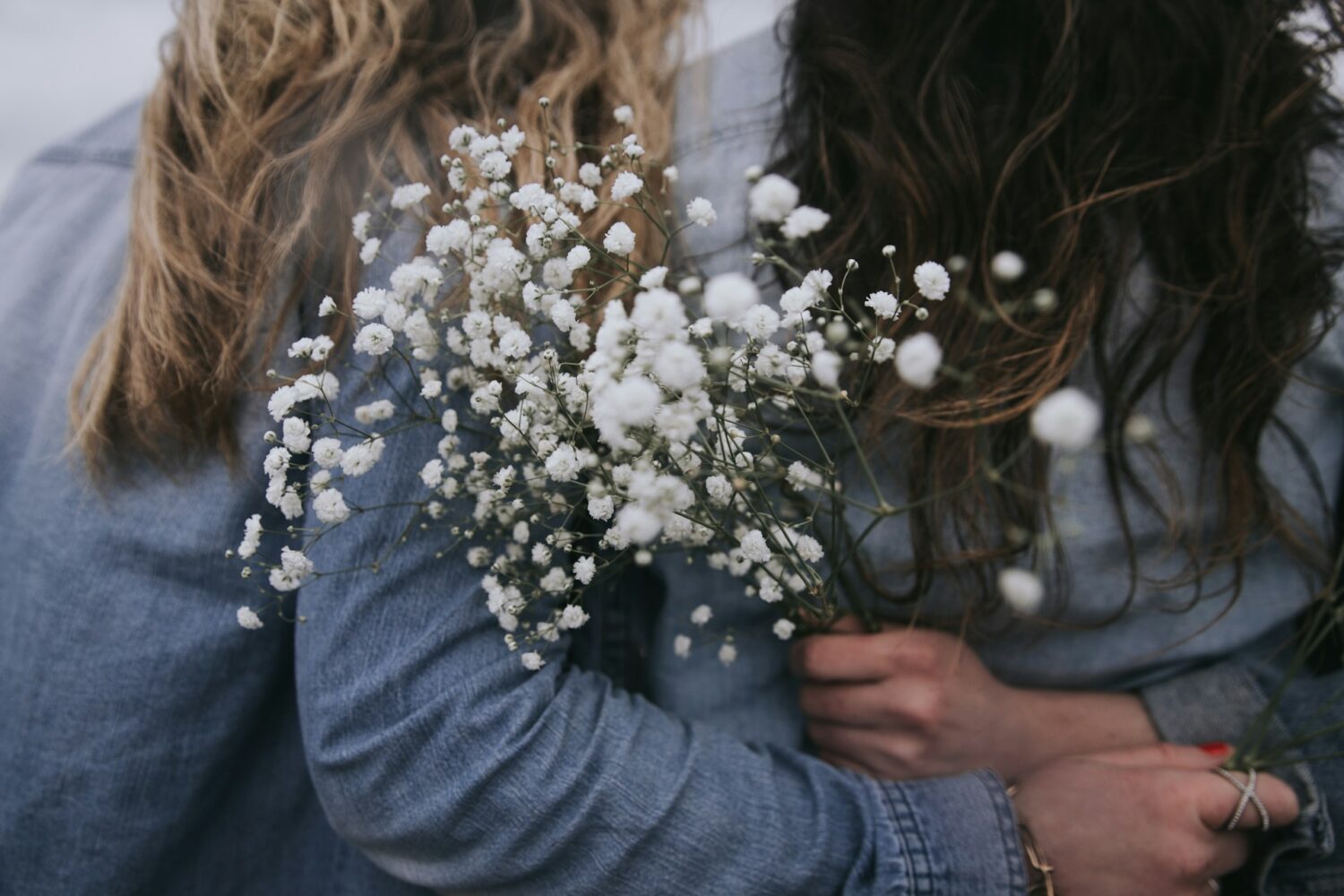 Two women with their arms around each other's backs, holding white flowers