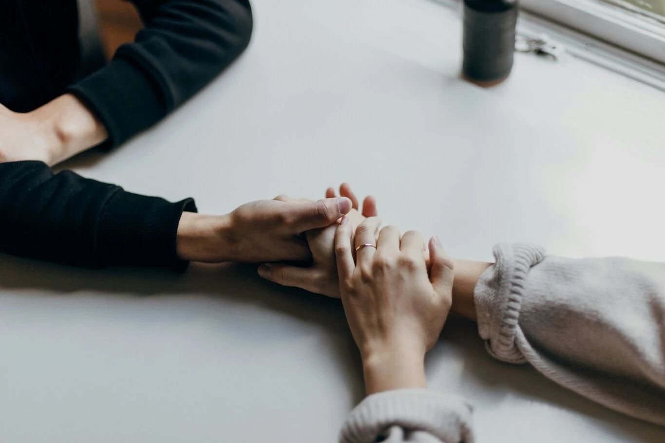 Two people holding hands across a table during a conversation.