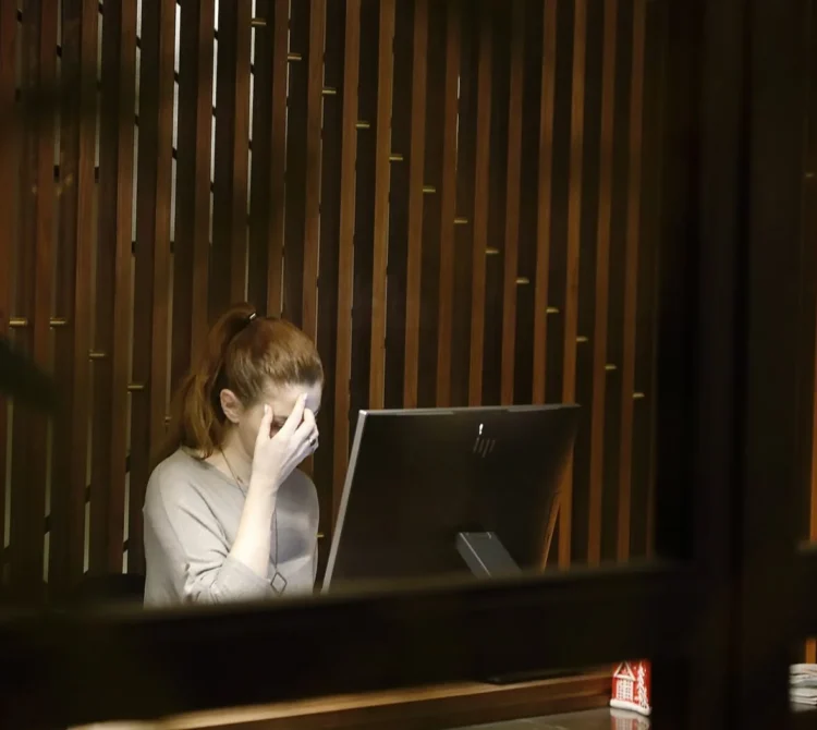 Woman sitting at a desk with one hand covering part of her face while using a desktop computer.