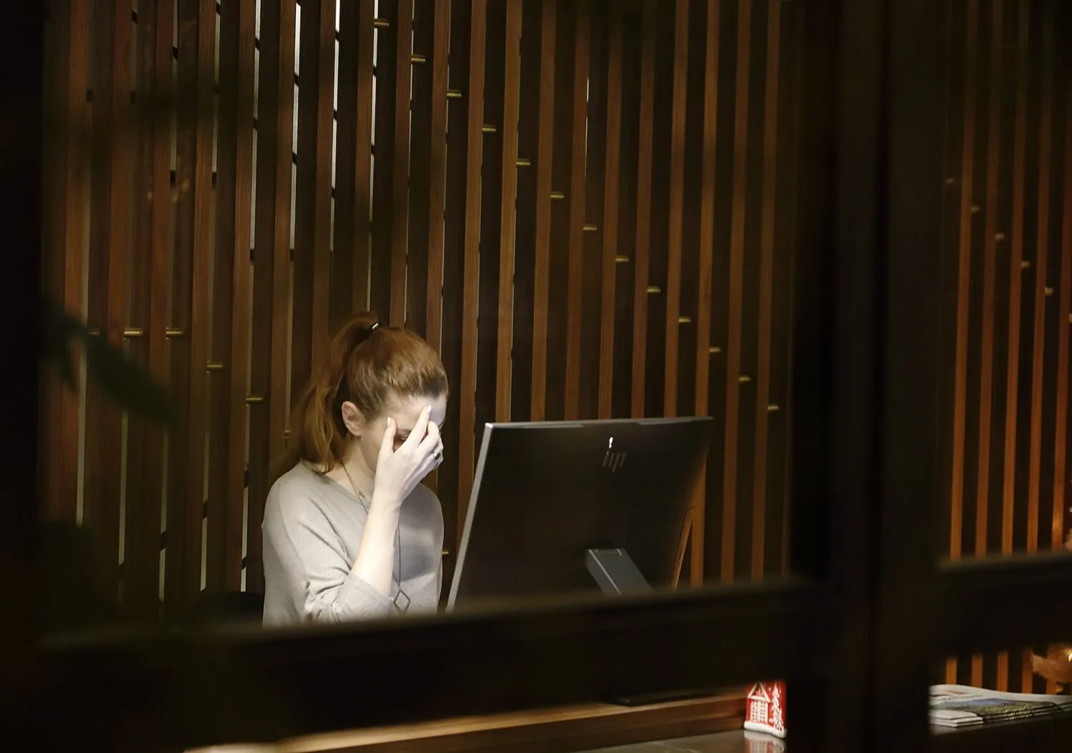 Woman sitting at a desk with one hand covering part of her face while using a desktop computer.