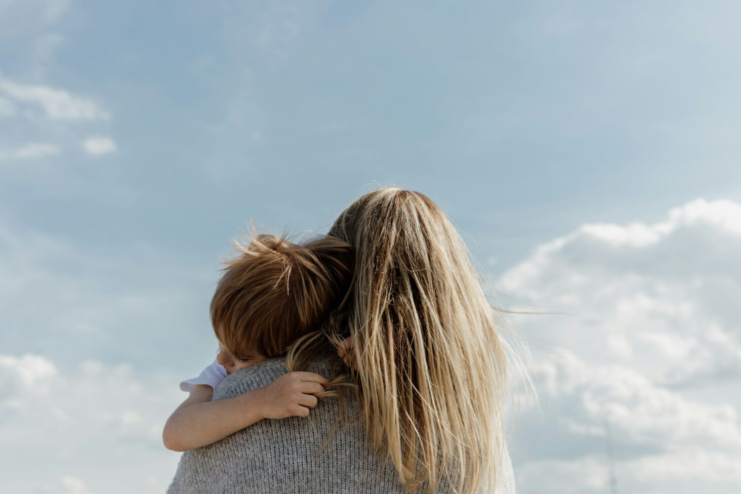 A woman holding a child in her arms, in front of a blue sky