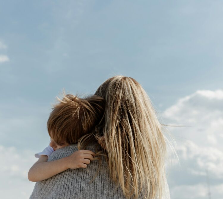 A woman holding a child in her arms, in front of a blue sky