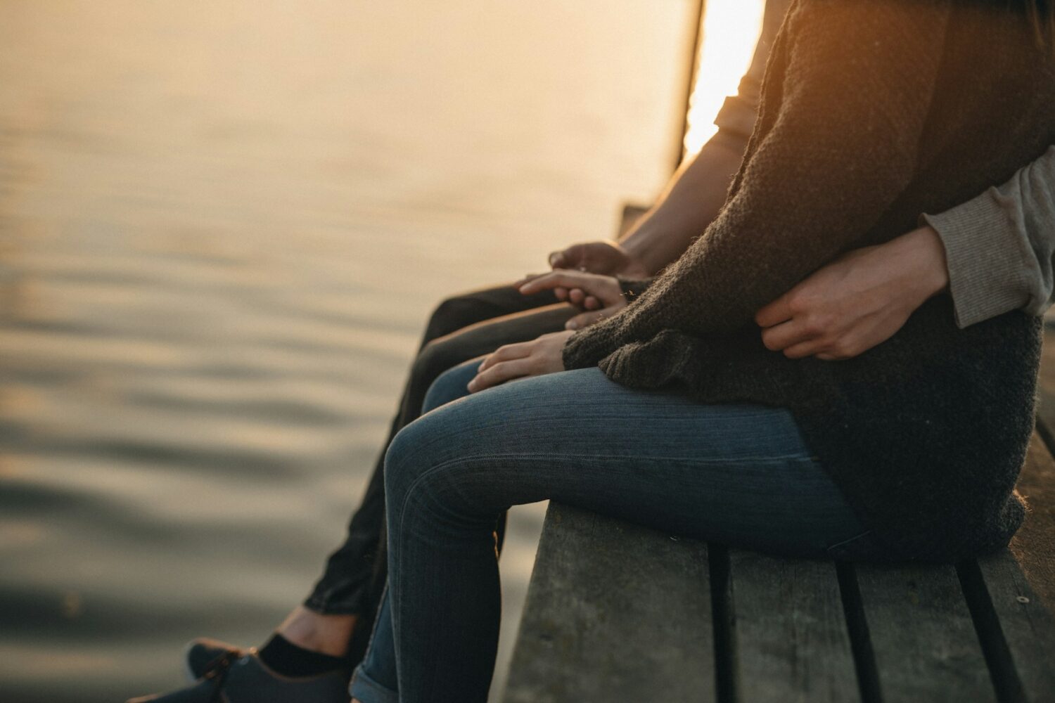 Couple sitting on wharf with legs dangling over the edge.