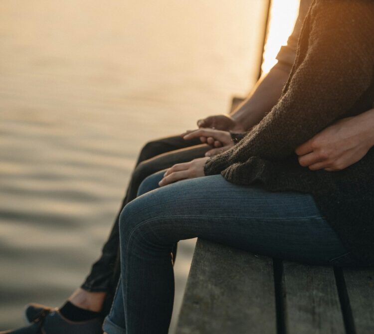 Couple sitting on wharf with legs dangling over the edge.