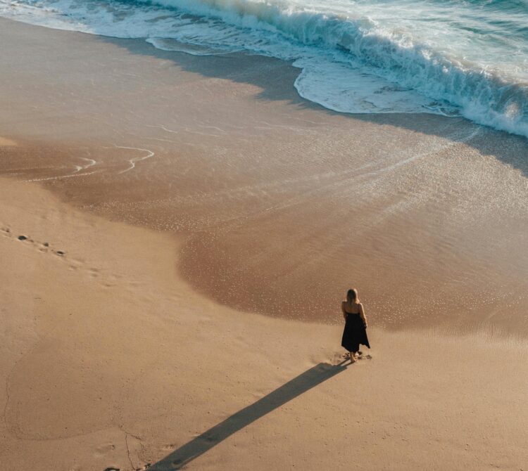 A view of a beach from above, with a women standing at the edge of the waves watching the water