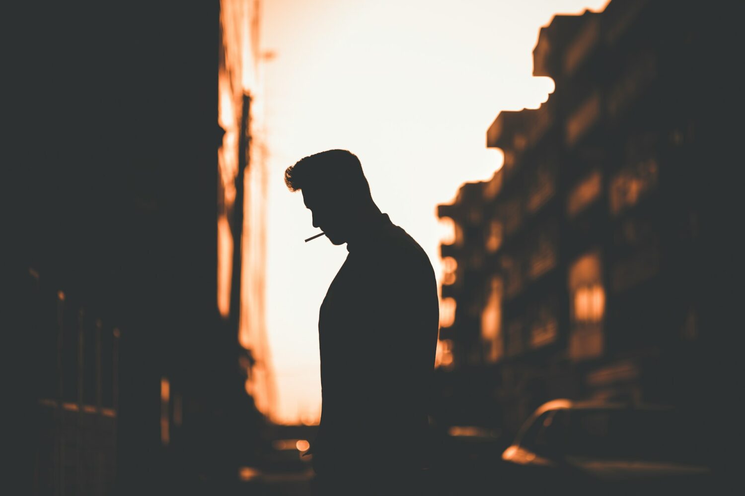 A man smoking outside silhouetted by the sunset