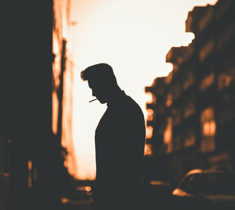 A man smoking outside silhouetted by the sunset