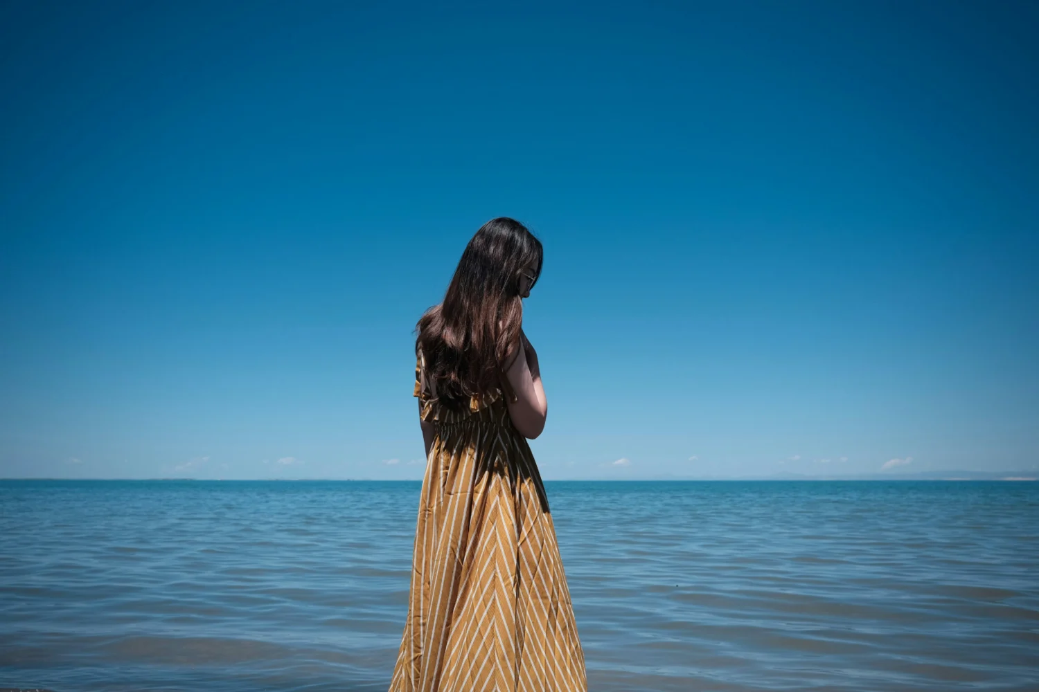 Young women standing by the blue water looking out to the ocean