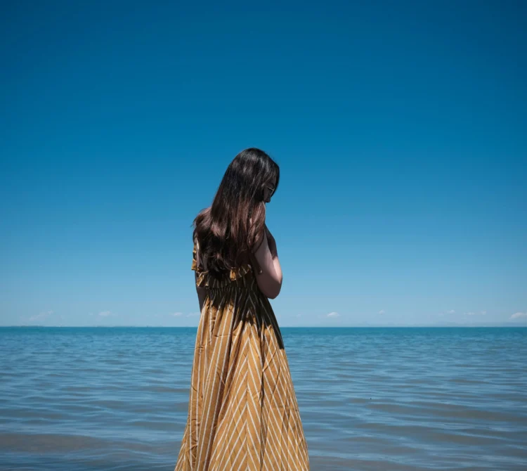 Young women standing by the blue water looking out to the ocean