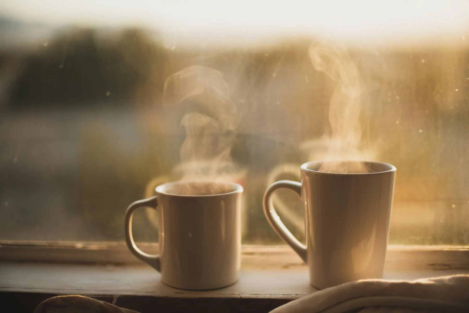 Two mugs on a window sill with steam floating up
