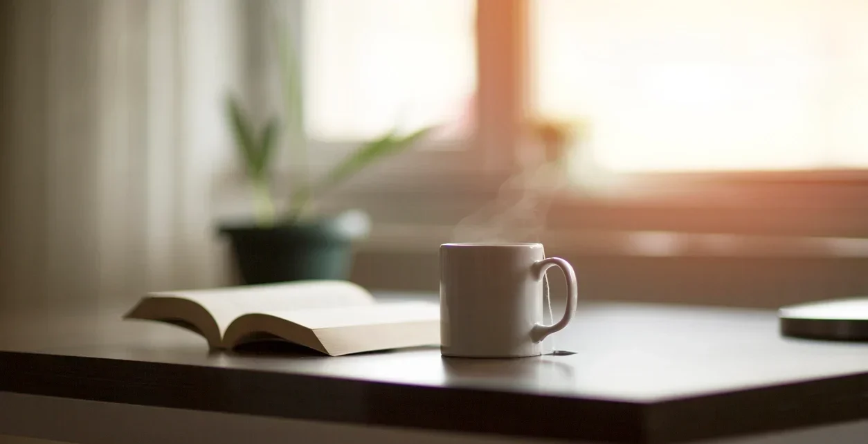 Book and coffee mug on a desk by a window