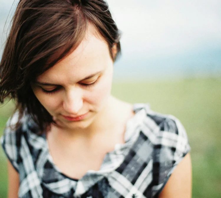 Women standing in grass field looking downwards with sad expression