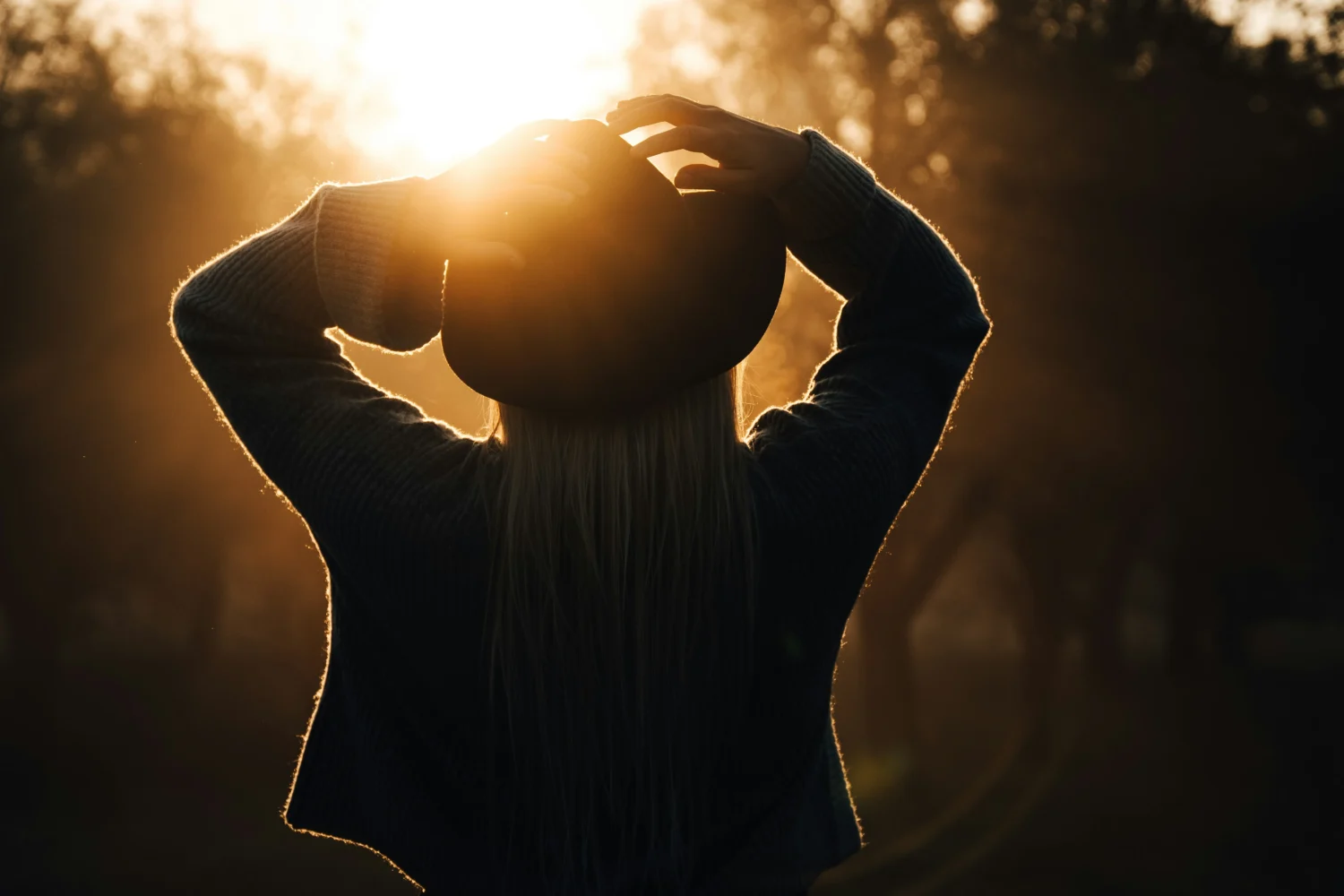 A woman standing facing the morning sun with her hands on her head