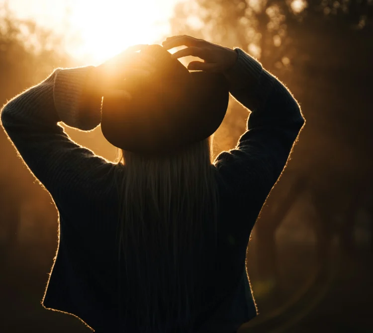 A woman standing facing the morning sun with her hands on her head