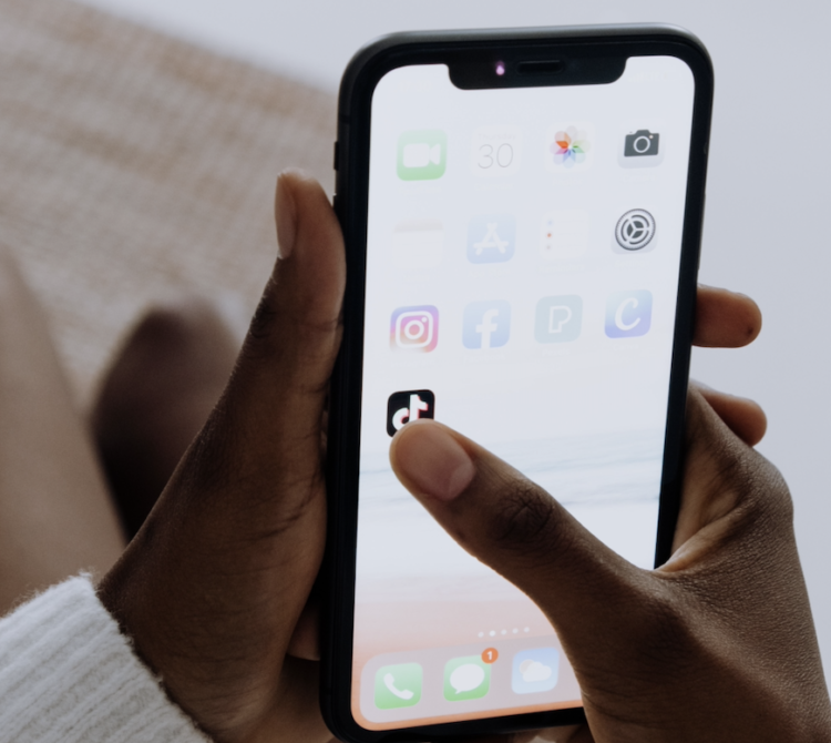 Close-up of a person holding a smartphone and tapping the TikTok app, with other social media apps visible on the screen