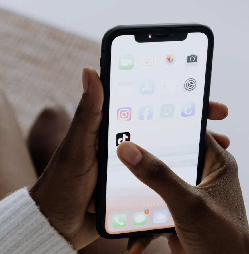 Close-up of a person holding a smartphone and tapping the TikTok app, with other social media apps visible on the screen