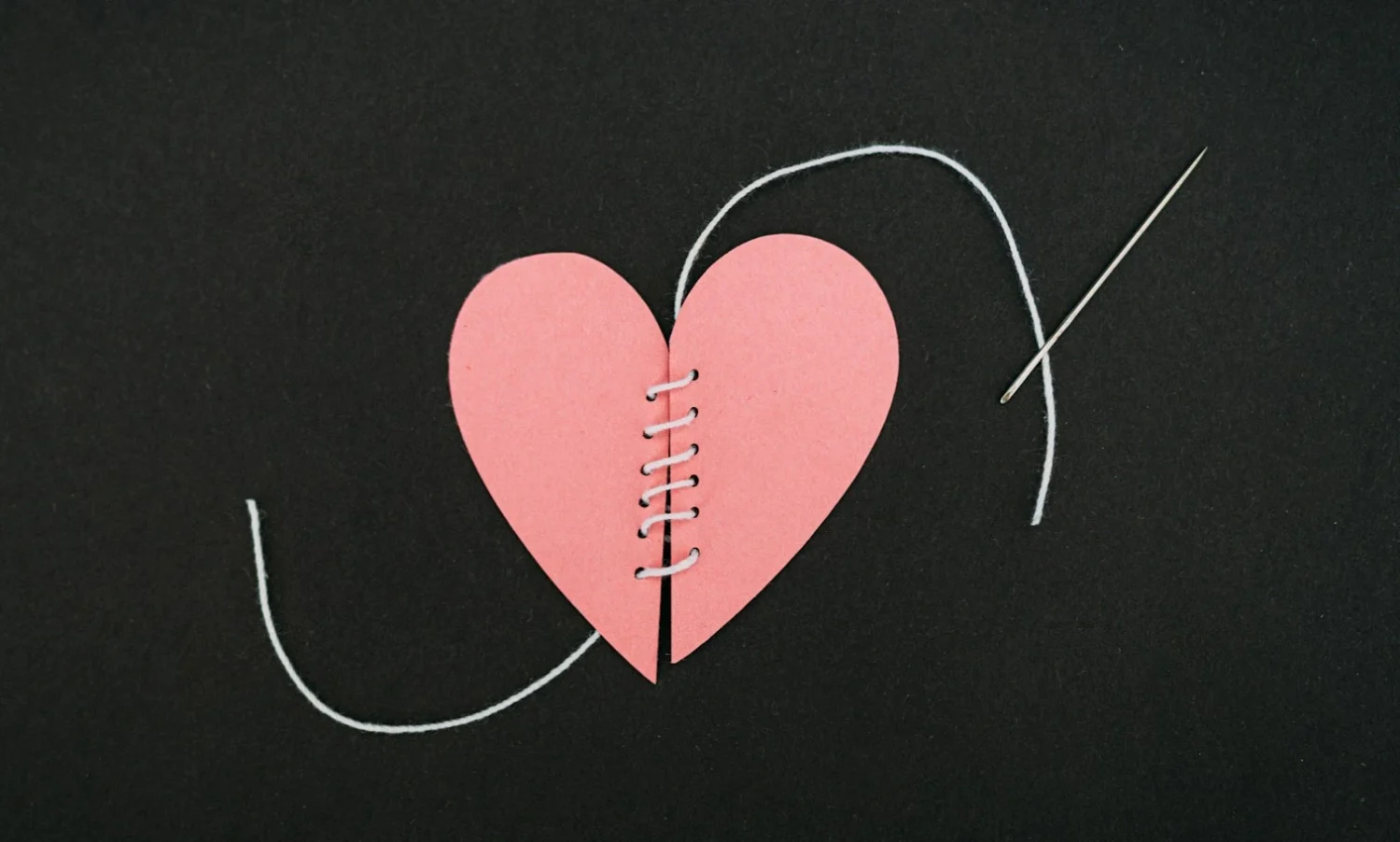 A pink paper heart that has been cut in two, sewn back together