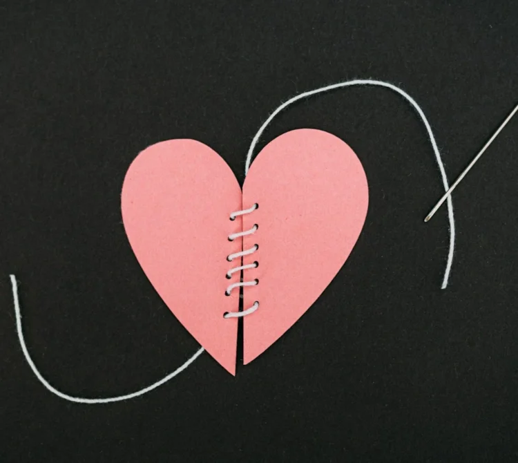A pink paper heart that has been cut in two, sewn back together