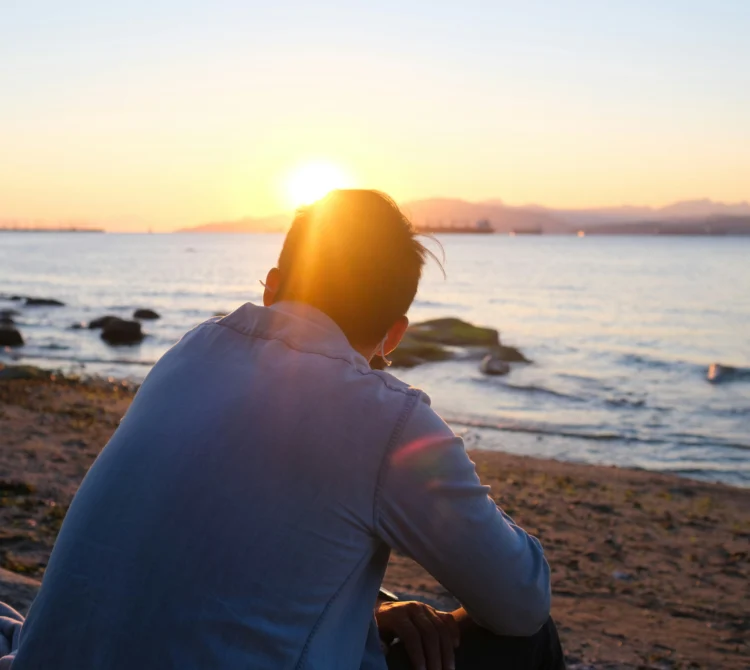 back of man sitting at the beach in contemplative way