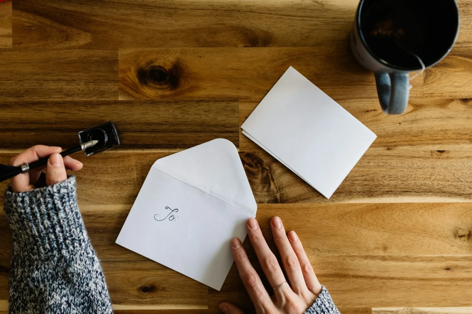 An overhead view of envelope and card on a table with someone about to write a letter