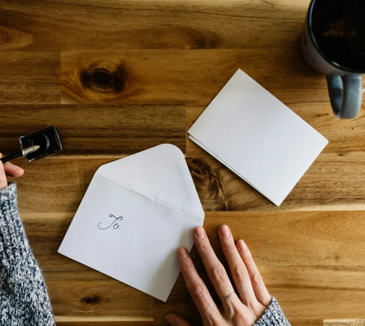 An overhead view of envelope and card on a table with someone about to write a letter
